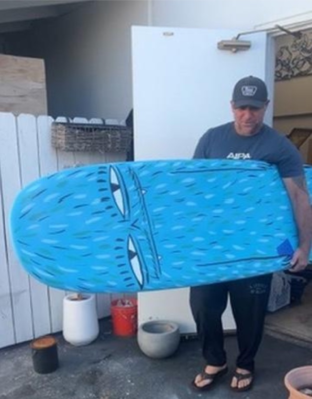 Duke Aipa holding the hand-painted blue KA Log surfboard