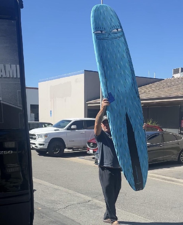 Duke Aipa holding the KA Log surfboard overhead on a sunny street